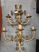 A GILT METAL WALL BRACKET WITH SIX CANDLE NOZZLES IN TWO TIERS OF THREE ON ARMS ATTACHED TO A BACK