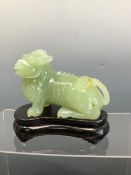 AN ORIENTAL CARVED JADE GREEN HARDSTONE FIGURE OF A GRIFFIN ON A WOODEN BASE.