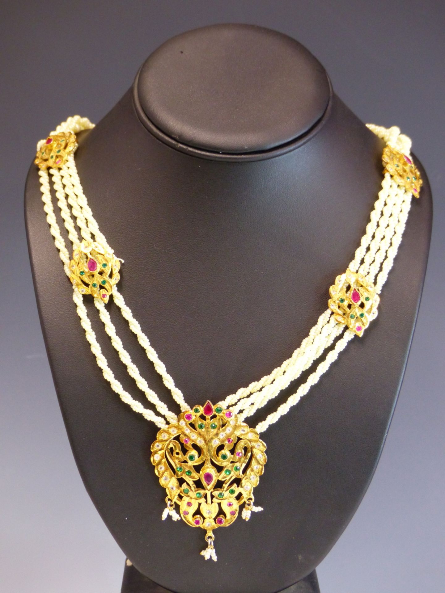 AN EASTERN NECKLACE THE GILDED PENDANT SET WITH COLOURED PASTE STONES SUSPENDED ON A WOVEN PEARL