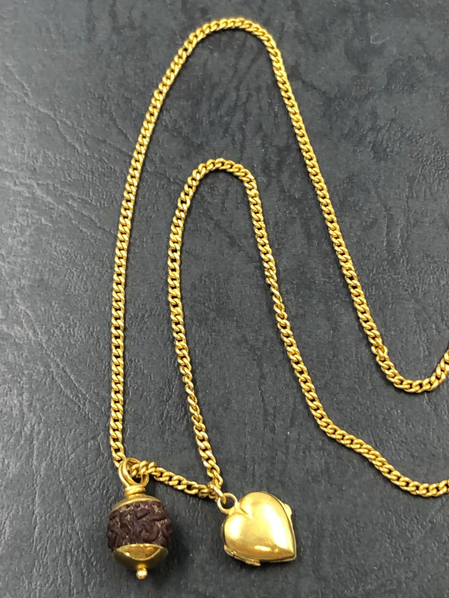 A CONTINUOUS 64cm NECK CHAIN STRUNG WITH CARVED BEAD PENDANT AND A SMALL HEART LOCKET, NO ASSAY