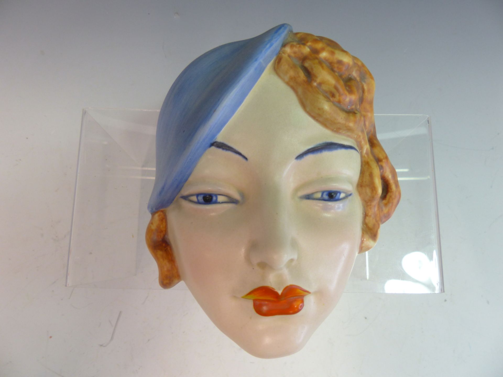 AN ART DECO POTTERY WALL MASK OF A YOUNG WOMAN WITH BLUE HAT. PROBABLY BY BESWICK. IMPRESSED MARKS