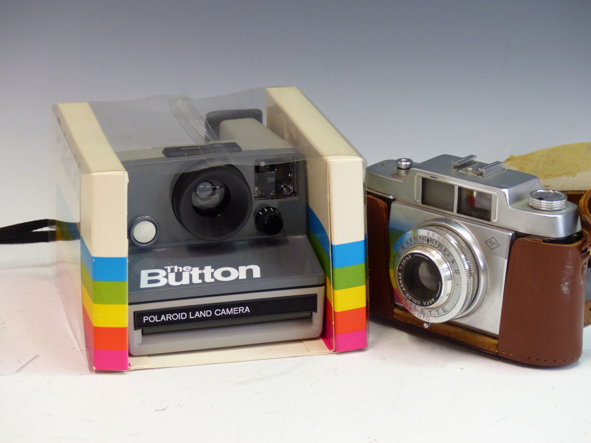A POLAROID LAND CAMERA "THE BUTTON" IN ORIGINAL PACKAGING WITH MANUAL. TOGETHER WITH AN AGFA SILETTE