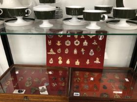 CAP BADGES: TWO GLAZED TABLE TOP DISPLAY CASES OF CAP BADGES TOGETHER WITH A RED VELVET PANEL