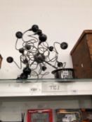 AN ELECTRIC CHANDELIER WITH MULTIPLE BLACK SHADED LIGHTS ON WIRES SCROLLING FROM A CENTRAL SPHERE