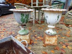 A PAIR OF PAINTED CAST IRON URNS ON SQUARE PLINTH BASES.