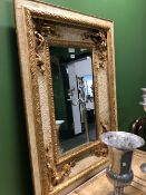 A RECTANGULAR MIRROR IN A CREAM PEBBLE DASHED FRAME GILT WITH VINE SPANDRELS. 117 x 88cms.