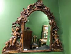 A FAUX WALNUT BAROQUE STYLE OVERMANTEL MIRROR, THE SHELL CRESTING ABOVE AMORINI SEATED EITHER SIDE