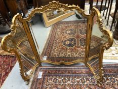 A THREE FOLD BEVELLED GLASS DRESSING TABLE MIRROR WITHIN A GILT ROCOCO FRAME CARVED WITH ROCAILLE