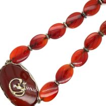 A CARNELIAN OVAL FLAT BEADED NECKLACE WITH A CENTRAL LARGER OVAL PANEL WITH APPLIED DRAGON MOTIF.