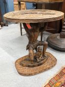 DICK IDEHEN, IBADAN, A CARVED WOOD COFFEE TABLE, THE CIRCULAR TOP SUPPORTED BY A WARRIOR ON ONE