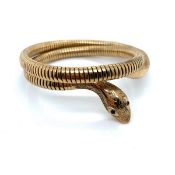 A 9ct HALLMARKED GOLD COILED SERPENT BANGLE THE HEAD SET WITH GARNET EYES. THE BANGLE WITH STEEL