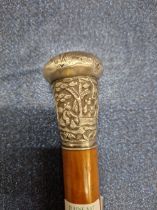 A WALKING CANE WITH A CHINESE WHITE METAL HANDLE WORKED WITH FIGURES UNDER TREES