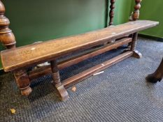 AN OAK BENCH SUPPORTED AT THE NARROW ENDS ON TURNED COLUMNS JOINED AT THE FEET BY A BAR STRETCHER