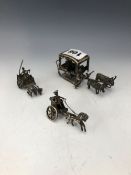THREE WHITE METAL MINIATURE CARTS, ONE DRAWN BY THREE DOGS, ANOTHER BY A HORSE AND THE LARGEST A