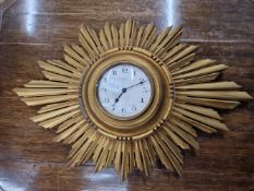 AN EARLY 20TH CENTURY CARVED GILTWOOD SUNBURST WALL CLOCK WITH WHITE ENAMEL DIAL.