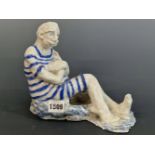 A STUDIO POTTERY FIGURE OF A MAN SEATED WEARING A BLUE STRIPED BATHING SUIT. W 22cms.