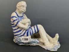A STUDIO POTTERY FIGURE OF A MAN SEATED WEARING A BLUE STRIPED BATHING SUIT. W 22cms.