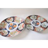 Two Japanese porcelain chargers with polychrome designs of island scenes and flowers, largest 40cm