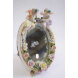 Small porcelain dressing table mirror of oval shape, the mirror surmounted by two cherubs with
