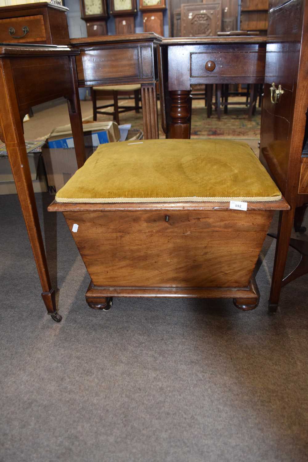 19th Century storage footstool with upholstered hinged lid over a tapering body raised on casters,
