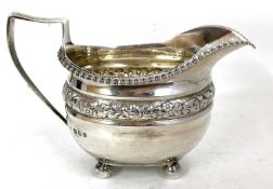 A George V silver cream jug of oval form having a gadrooned border and a band of flowers and