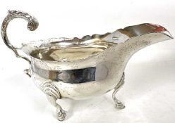 An early 20th Century silver sauce boat of typical form with a wavey rim and a flying leaf capped