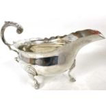 An early 20th Century silver sauce boat of typical form with a wavey rim and a flying leaf capped