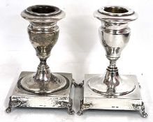 A pair of white metal dwarf candlesticks of urn shape on ring turned stems to a square base on