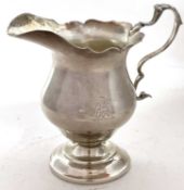 A George V silver cream jug in 18th Century style with card cut rim, leaf capped scroll handle and