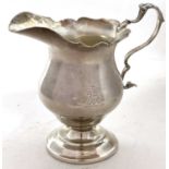 A George V silver cream jug in 18th Century style with card cut rim, leaf capped scroll handle and