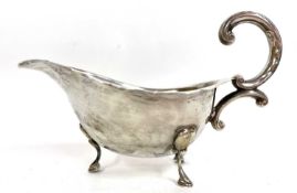 Silver sauce boat of typical form, card cut rim and flying scroll leaf handle, supported on three
