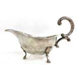 Silver sauce boat of typical form, card cut rim and flying scroll leaf handle, supported on three