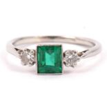 Precious metal emerald and diamond ring, the step cut emerald flanked by two small round cut