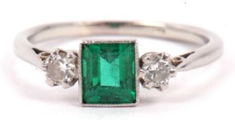 Precious metal emerald and diamond ring, the step cut emerald flanked by two small round cut