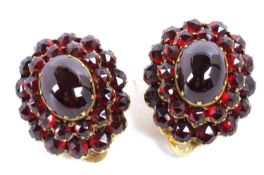 A pair of garnet cluster earclips, the central oval garnet cabochon surrounded by faceted garnets,