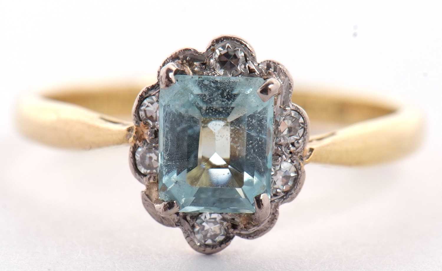 An 18ct aquamarine and diamond ring,the emerald cut aquamarine surrounded by small single cut