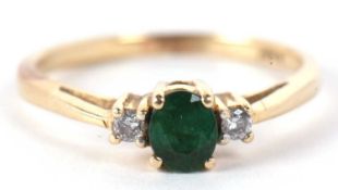 An emerald and diamond ring, the central round emerald set to either side with a small round