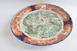 A large Japanese porcelain charger with central panel famille vert of a scrolling dragon within