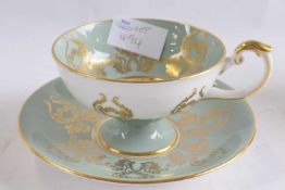 An Aynsley cup and saucer with a gilt design on light green ground, the cup with fruit decoration