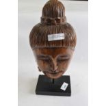 A carved wooden head on black rectangular stand