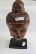 A carved wooden head on black rectangular stand
