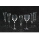 A group of glass ware including five champagne flutes raised on knop and straight stem with engraved