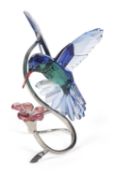 A Swarovski model of a hummingbird in blue and green hovering above a pink flower, 16cm high