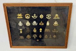 A framed and glazed display of various military cap badges and insignias