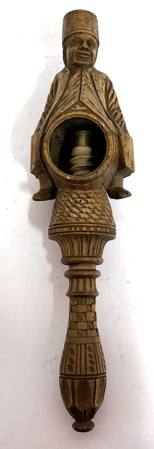 An antique treen box wood nut cracker, a carved figure sitting astride a barrel with screw handle,