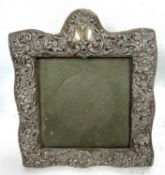 An Edwardian silver photograph frame, square form with arched top and plain cartouche, embossed with
