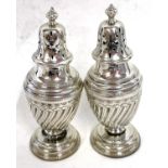 A pair of Victorian silver peppers, the urn shaped bodies with a wrythen design having urn finials