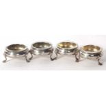 Four George III silver cauldron salts, raised on three hoof feet with later clear glass liners,