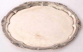 A George V silver salver, of shaped circular form with raised gadrooned rim and a shall border,