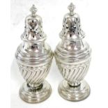 A pair of Victorian silver peppers, the urn shaped bodies with a wrythen design having urn finials